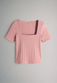 Top rosa a coste con maniche corte e scollo quadrato, appoggiato in piano su uno sfondo neutro.