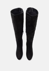 Paire de bottes hautes en daim noir avec fermetures éclair latérales, bouts arrondis et un design légèrement décontracté sur fond blanc.