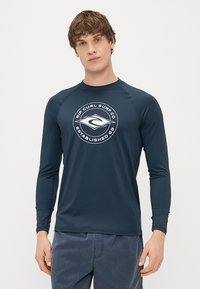 Ναυτικό μακρυμάνικο rash guard με στρογγυλό λογότυπο στο στήθος. Φτιαγμένο από ελαστικό ύφασμα, διαθέτει ραφές raglan και λεία υφή.
