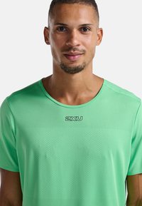 Camiseta atlética de manga corta verde, hecha de una tela transpirable, con un patrón texturizado y un logo negro "2XU" en el pecho.