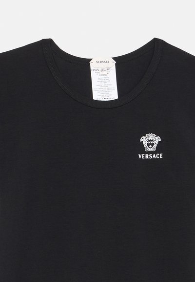 Μαύρο μπλουζάκι Versace με λευκό λογότυπο Medusa και όνομα της μάρκας στην αριστερή πλευρά του στήθους και ορατή ετικέτα φροντίδας μέσα στο γιακά.
