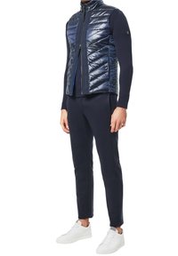 Marinblå puffer väst med horisontell quiltad mönster, hög krage och dragkedja fram. Kombinerad med marinblå byxor och vita sneakers. Slät textur.