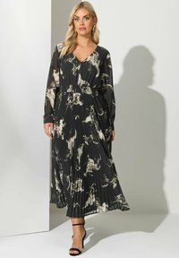Svart plisserad klänning med abstrakta mönster i beige och kräm, långa ärmar, V-ringning, elastisk midja, kombinerad med svarta sandaler med remmar.