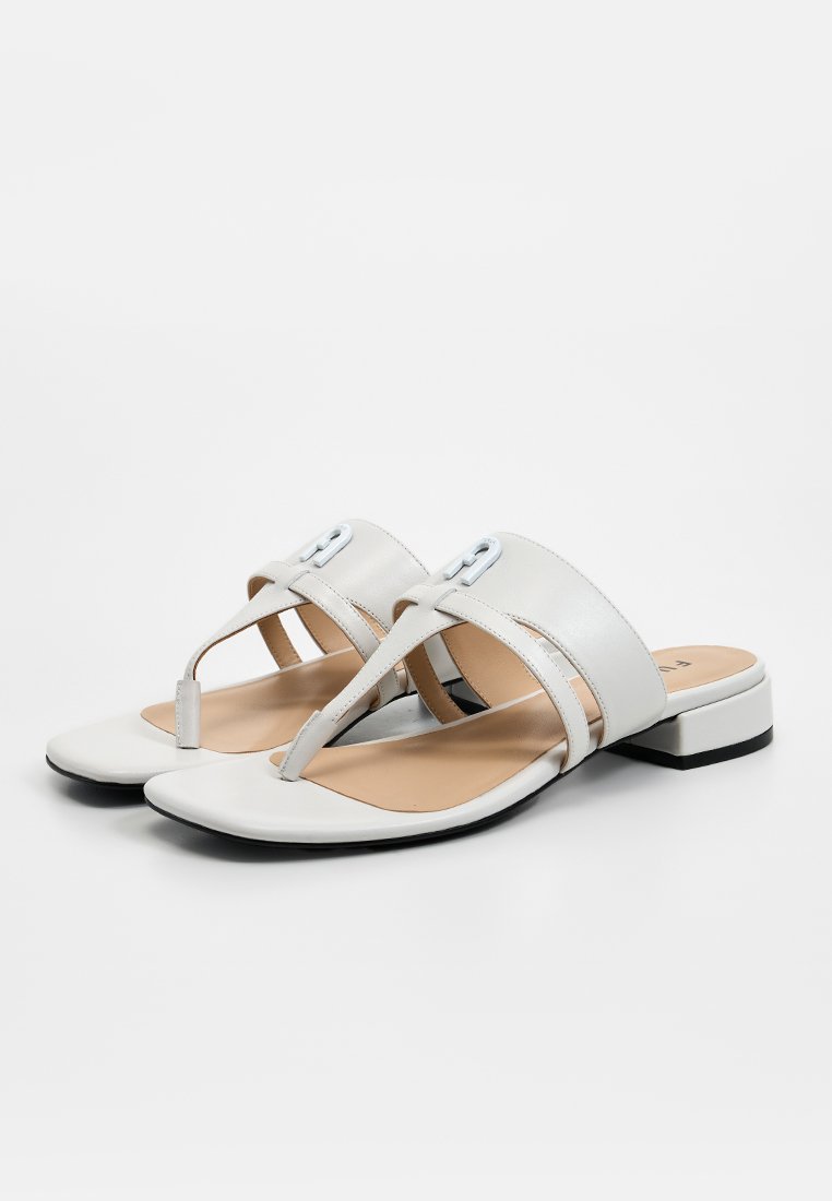 Sandalias de cuero blanco con tacón bajo, diseño en forma de T, tiras cruzadas y una pequeña hebilla decorativa en la parte superior. Textura suave.