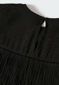 Tissu texturé noir avec un petit bouton et une fermeture par boucle au-dessus d'un matériau finement plissé, montrant le détail de l'encolure d'une robe ou d'un haut.