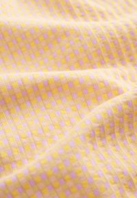 Tissu doux avec une texture côtelée présentant un petit motif à carreaux en jaune, rose clair et beige.