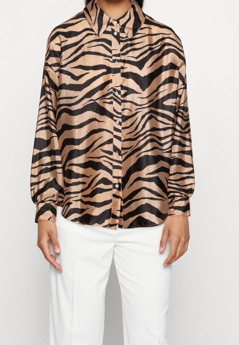 Brown and black striped shirt with a shiny texture, featuring a collar, button front, and long sleeves, paired with white trousers.