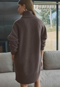 Brun oversized sweaterklänning med hög ribbad krage, långärmad med ribbade ärmslut, tillverkad av mjukt, texturerat tyg.