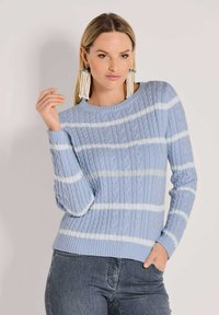 Lichtblauwe cable-knit trui met witte strepen, wijde halslijn, geribbelde mouwen en zoom, gedragen met een blauwe spijkerbroek.