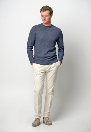 Blauwe gebreide trui met een ronde halslijn, crème broek en beige sneakers. Zachte textuur, slim fit ontwerp en neutraal kleurenpalet.