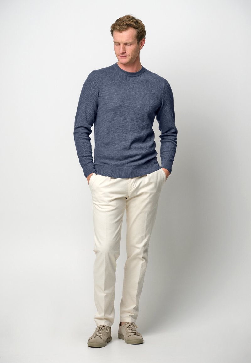 Pull en tricot bleu avec un col rond, pantalon crème et baskets beiges. Texture douce, conçue à la coupe ajustée, et palette de couleurs neutres.