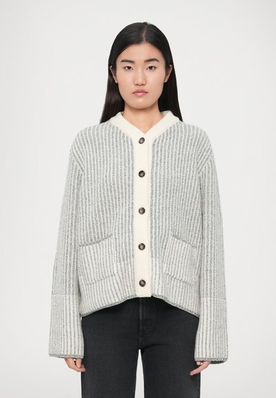 Cardigan gris et crème à rayures verticales, col en V, cinq boutons et deux poches avant. Tissu semblant doux et texturé.