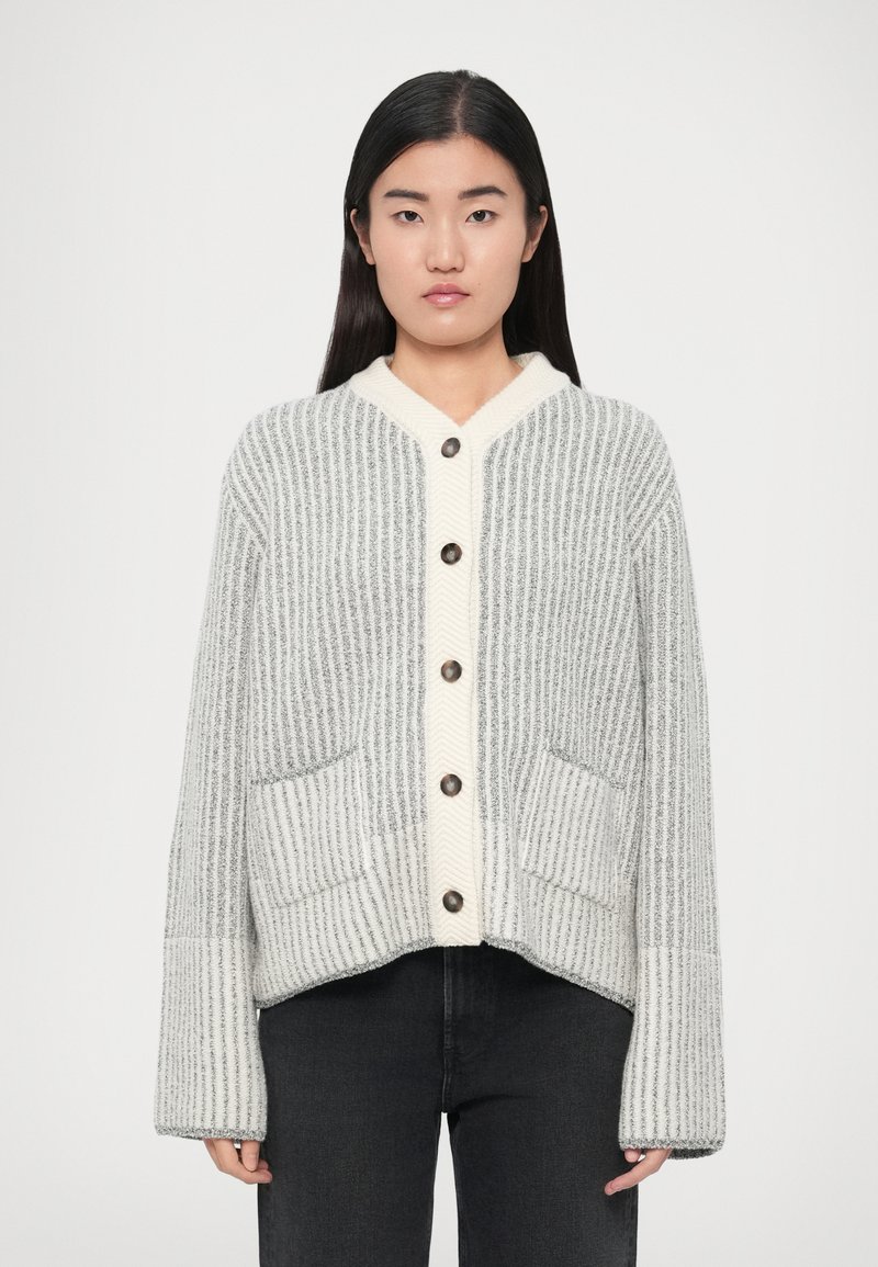 Γκρι και κρεμ ζακέτα με κάθετες ρίγες, ντεκολτέ σ�ε σχήμα V, πέντε κουμπιά και δύο μπροστινές τσέπες. Το ύφασμα φαίνεται μαλακό και με υφή.