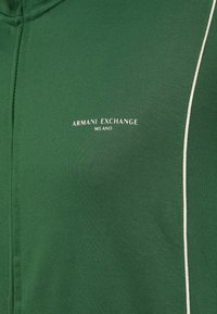 Zöld pulóver puha anyagból, fehér cipzárral, az „Armani Exchange Milano” logóval a mellkason.
