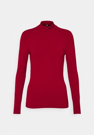 Maglione a maniche lunghe rosso con collo alto realizzato in tessuto morbido. Presenta un design aderente e un logo sottile sul collo. Texture liscia.