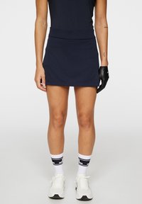 Marinblå idrotts-kjol med en åtsittande midja, tillverkad av ett slätt tyg. I kombination med vita strumpor med en svart rand och vita sneakers.