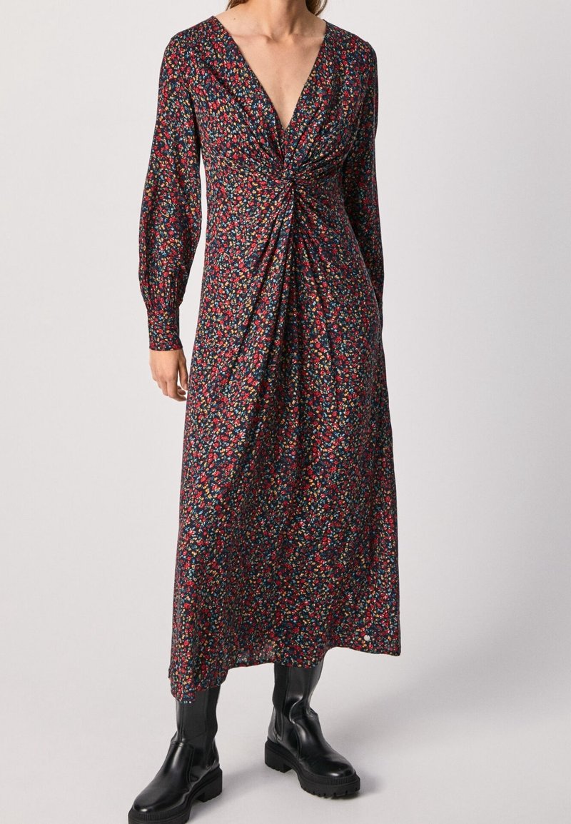 Robe longue à manches longues ornée de fleurs, avec un décolleté en V profond, présentant un détail torsadé à la taille. Le motif se compose de petites fleurs multicolores sur un fond sombre.
