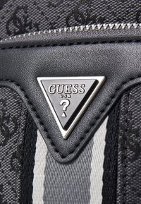 Cartera de imitación cuero negra con superficie texturizada, herrajes en tono plateado, logotipo triangular prominente y acentos en blanco y negro a rayas.