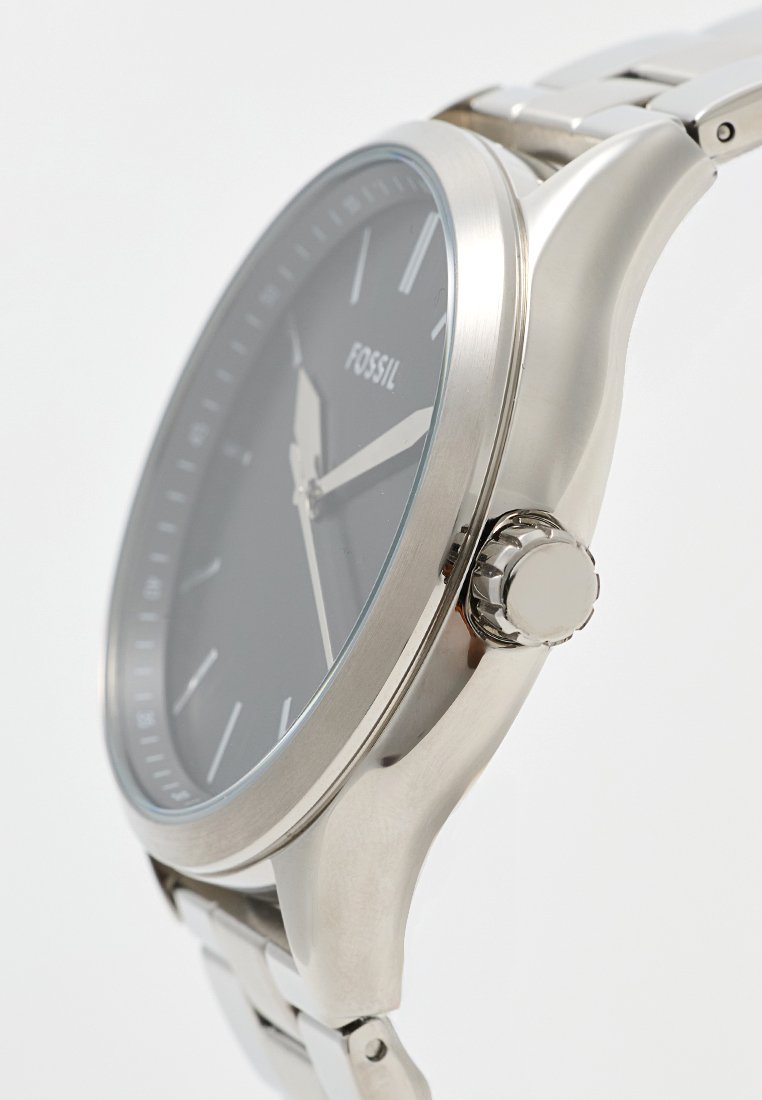 Montre ronde en métal argenté avec un cadran noir, des index argentés et une finition poli. Elle possède une couronne texturée et un bracelet en métal.