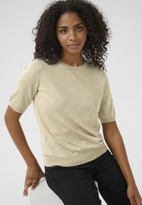 Beež lühikeste varrukatega kampsun ümmarguse kaelusega ja õrna tekstuuriga; kantud mustade pükstega, luues lõdvestunud sobivuse.