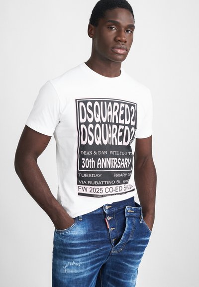 T-shirt en coton blanc avec un texte graphique noir et rose audacieux annonçant un événement pour le 30ème anniversaire, associé à un jean en denim bleu.