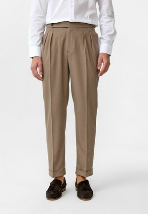 Beige plooiebroek met een geribbelde textuur, voorzien van een manchetzoom en zijzakken, gecombineerd met zwarte loafers en een wit shirt.