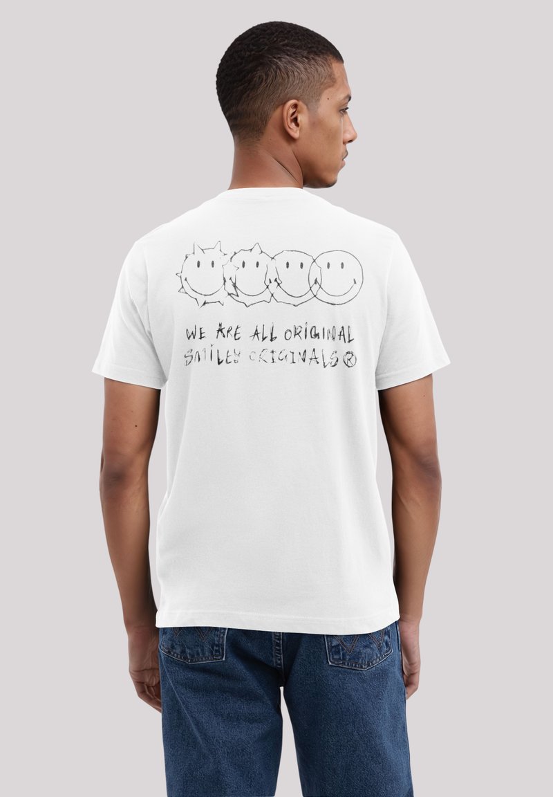 White cotton t-shirt featuring a graphic of four smiley faces and the text "WE ARE ALL ORIGINAL SMILEY ORIGINALS" in black ink.