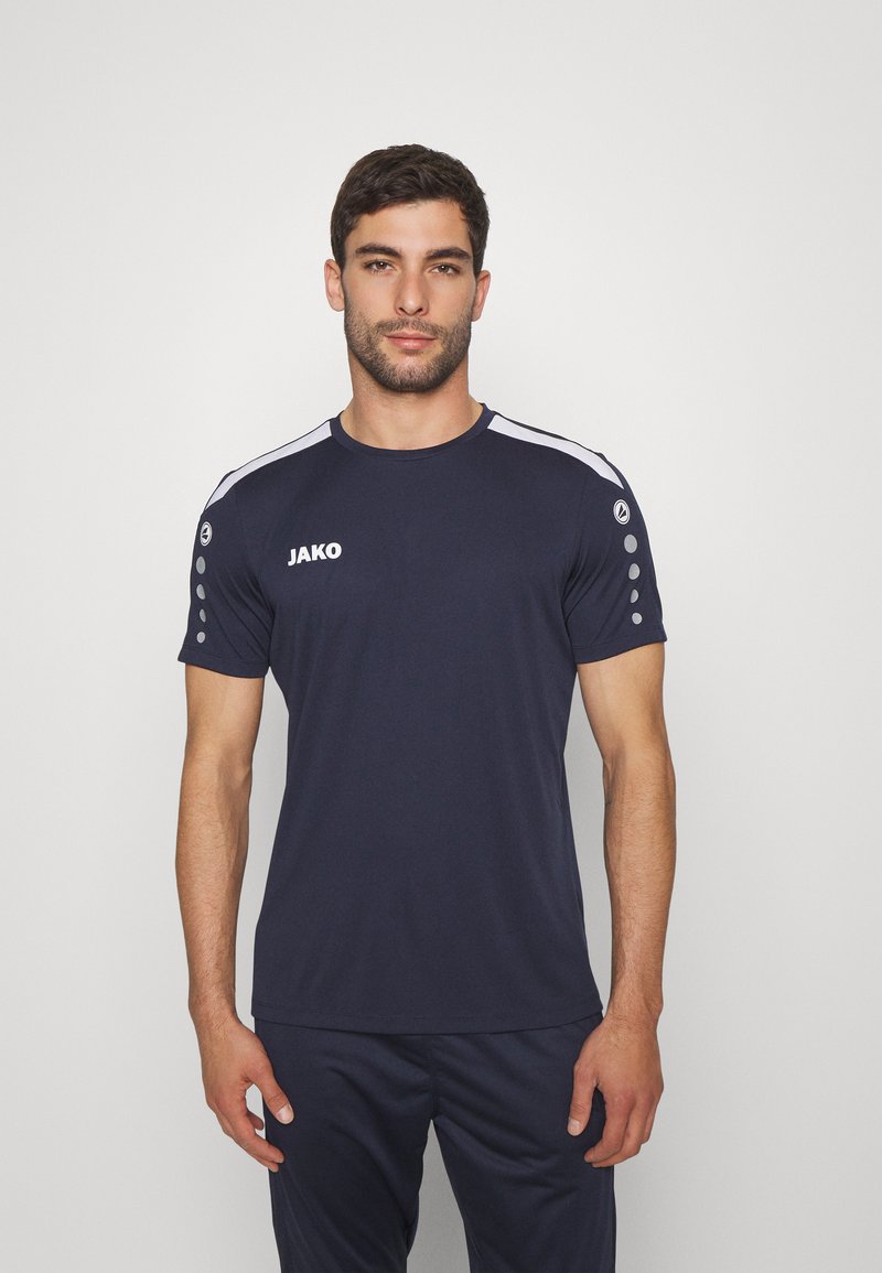 T-shirt sportivo navy a maniche corte, con logo JAKO, strisce bianche sulle spalle e collo rotondo. Presenta punti grigi sulle spalle.