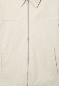 Lichtbeige zip-up jas met een puntige kraag, twee zijzakken en een soepele, licht gestructureerde stof. Eenvoudig en modern ontwerp.