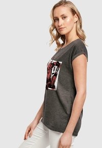 Grå kortærmet t-shirt med et komikstil rødt grafisk print fortil. Blød tekstur, løs pasform, rund halsudskæring.