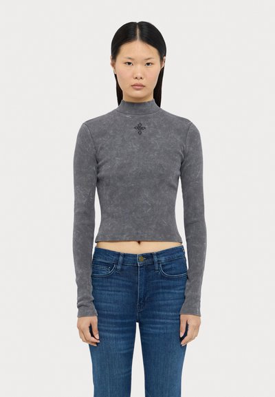 Grå ribbad långärmad crop top med hög hals och broderad detalj vid bröstet, ihopparat med mörkblå tajta jeans.