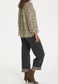 Blouse transparente à motif avec un dessin de vagues marron, associée à un jean foncé, ample, et des bottines marron à bout pointu et talon.