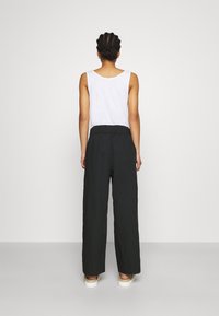 Pantalons larges noirs avec une taille élastique, associés à un top sans manches blanc, vus de dos sur un fond neutre.
