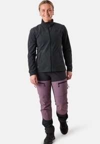 Giacca in pile con zip nera, dal design aderente. Abbinata a pantaloni bicolore viola e neri con tasche con zip. Calzature nere.