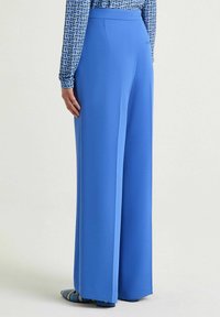 Pantaloni blu a vita alta con design a gamba larga, realizzati in tessuto liscio. Sul retro presentano una singola tasca e cuciture minimali.