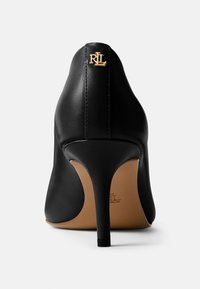 Fekete bőrből készült magassarkú cipő, hegyes orral, struktúrált felülettel és arany logó díszítéssel. Vékony tűsarkúval és világosbarna talppal rendelkezik.