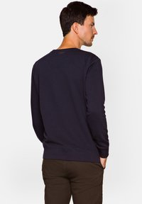 Granatowy sweatshirt z długim rękawem, okrągłym dekoltem, ściągaczami przy mankietach i dolnym brzegu. Wykonany z miękkiego materiału, z delikatnym brandingiem na tylnej części dekoltu.