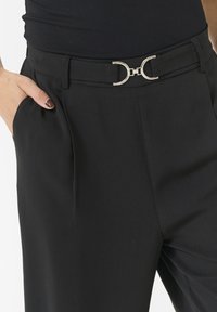 Schwarze maßgeschneiderte Hose mit einer eleganten silbernen runden Schnalle am Bund, glatter Textur und seitlichen Taschen.