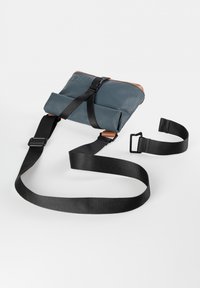 Graue wasserdichte Tasche mit aufgerolltem Verschluss, schwarzen verstellbaren Riemen und braunen Lederakzenten; minimalistisches Design, rechteckige Form.