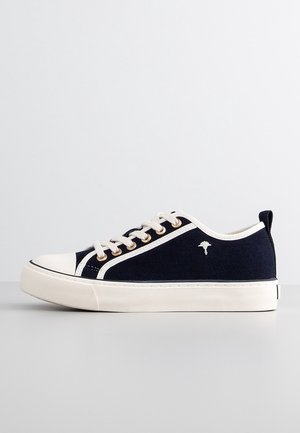 Baskets basses bleu marine avec semelle blanche, lacets, bout renforcé, bordure latérale et un petit logo fleur blanche sur le côté extérieur.