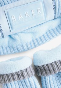 Svijetloplava flis kapa s rebrastim sivo-plavim pletenim pojasom, koji sadrži bijelu oznaku "BAKER BY TED BAKER". Mekana tekstura.