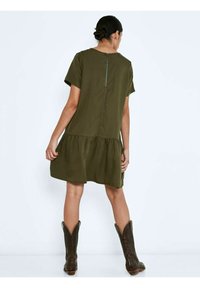 Vestido verde oliva de manga corta con dobladillo en capas, que presenta un zipper en la parte trasera. Llevado con botas de vaquero marrones, muestra un ajuste relajado y una textura suave.