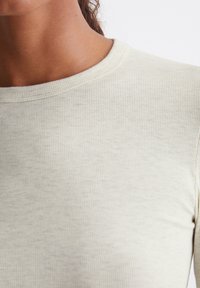 Lys beige ribbetopp med rund halslinning, som viser en jevn tekstur og subtile variasjoner i stoffets farge. Ingen synlige mønstre eller detaljer.