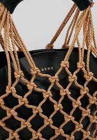 Černá kožená kabelka se uzlovým designem z hnědé šňůry. Má zaoblenou rukojeť a na přední straně zlaté logo "DKNY".