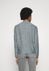 Light gray knitted jacket with a textured finish, featuring a round neckline and long sleeves, worn over gray jeans.
