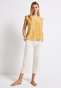 Top giallo senza maniche con un sottile motivo ondulato, abbinato a pantaloni larghi color crema con tasche. Sandali semplici completano l'outfit.