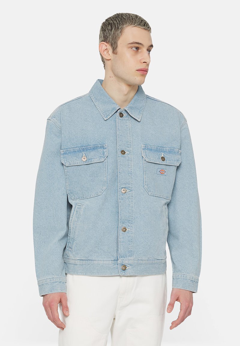 Ljusblå denimjacka med krage, två framfickor med lock, knappstängning, och en något kortad passform.