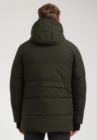 Giacca puffer verde scuro con cappuccio, caratterizzata da un design trapuntato, cuciture visibili e dettagli a coste sul colletto e sui polsini.