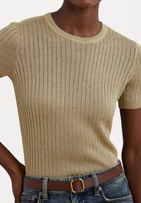 Top de malha de manga curta em dourado, com decote redondo. Usado com um cinto castanho e jeans de ganga, exibindo um design justo e uma textura suave.