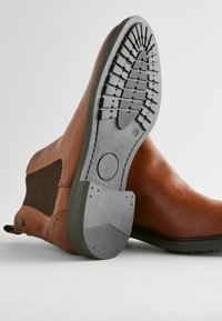 Botines de piel marrón con un empeine texturizado, detalle de malla a los lados y una suela de goma con un patrón estriado para mayor tracción.